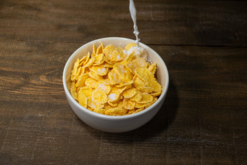 milk is poured into a plate with cornflakes on a wooden background