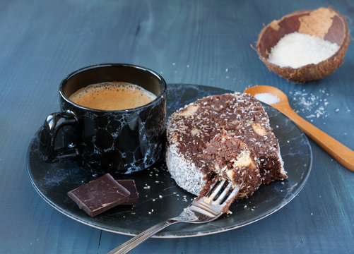 Chocolate biscuit salami with walnuts and coconut flakes with a cup of coffee on blue wooden table