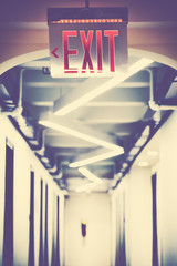 Emergency exit sign in empty corridor, selective focus, color toning applied.