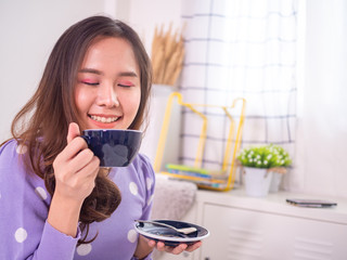 A woman with a soft smile and closed eyes, smelling the aroma from her cup in front.
