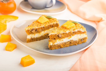 Homemade cake with persimmon and pumpkin and a cup of coffee on a white wooden background with orange textile. side view, selective focus.