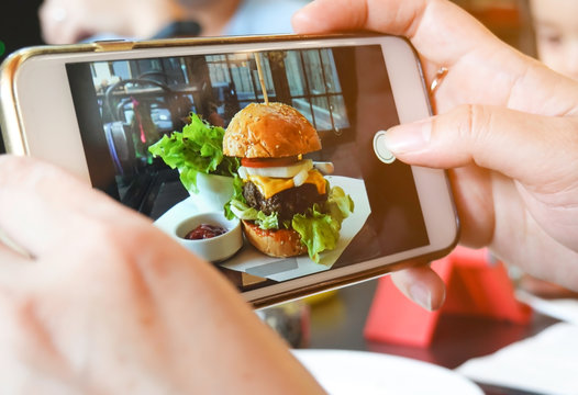 Selective focus smartphone picture which woman hands takes photography by smartphone of hamburger with fresh vegetables in the restaurant