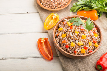 Buckwheat porridge with vegetables in wooden bowl on a white wooden background and linen textile. Side view, copy space, selective focus.