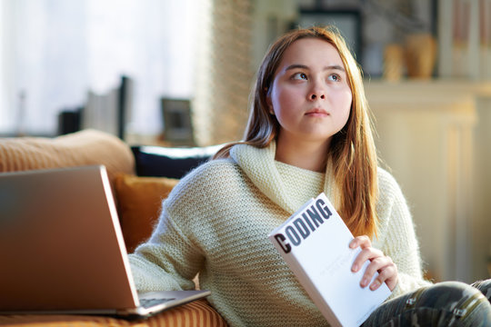 pensive teenager girl with laptop and book learning coding