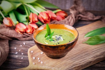 Homemade green spring cream soup with wild leek on a wooden background. Red orange tulips flowers