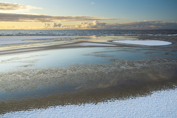 Sunrise light over the snowy beach of Baltic sea in winter morning, with the beautiful reflections of clouds in water