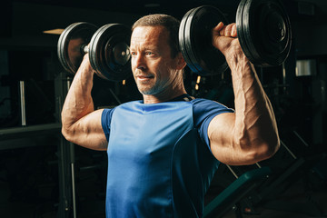 Fototapeta na wymiar Senior man in his fifties lifting weights in a gym