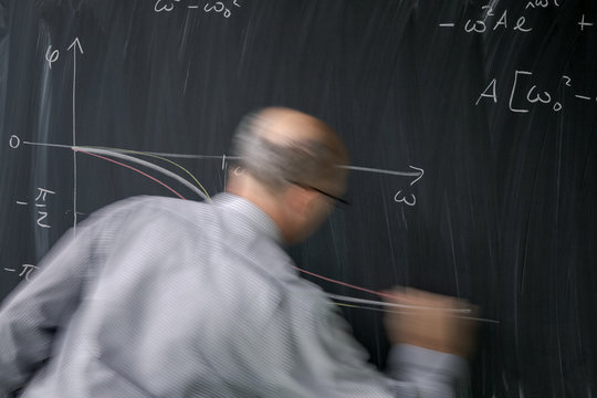 Math teacher drawing   fuction graph on a blackboard during mathclass (motion blurred image)