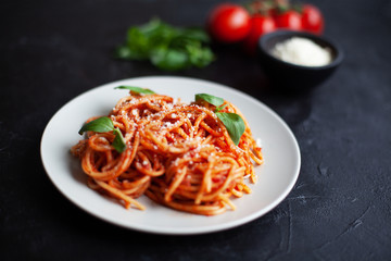 Tasty appetizing classic italian spaghetti pasta with tomato sauce, cheese parmesan and basil on plate on dark backgroound