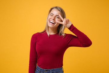 Laughing young blonde woman girl in casual clothes posing isolated on yellow orange background studio portrait. People emotions lifestyle concept. Mock up copy space. Showing victory sign, blinking.