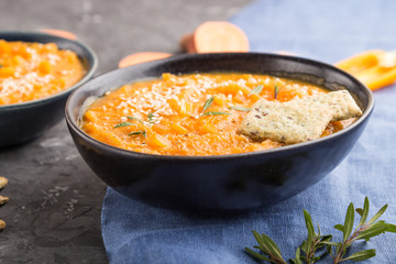 Sweet potato or batata cream soup with sesame seeds and snacks in blue ceramic bowls on a black concrete background. side view, selective focus
