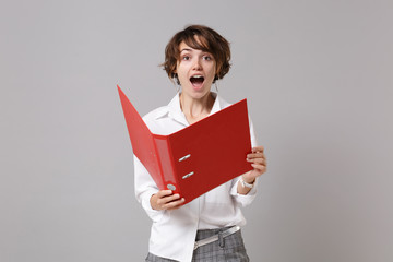 Obraz premium Excited young business woman in white shirt posing isolated on grey background studio portrait. Achievement career wealth business concept. Mock up copy space. Holding red folder for papers document.
