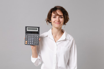 Smiling beautiful young business woman in white shirt posing isolated on grey wall background studio portrait. Achievement career wealth business concept. Mock up copy space. Hold in hand calculator.