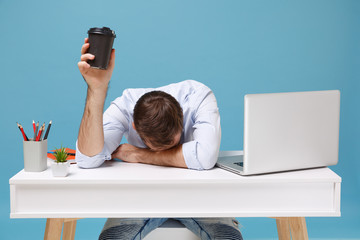 Tired young man in shirt sit and work at desk with pc laptop isolated on blue background....