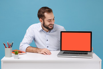 Cheerful young man in shirt sit at desk isolated on pastel blue background. Achievement business...