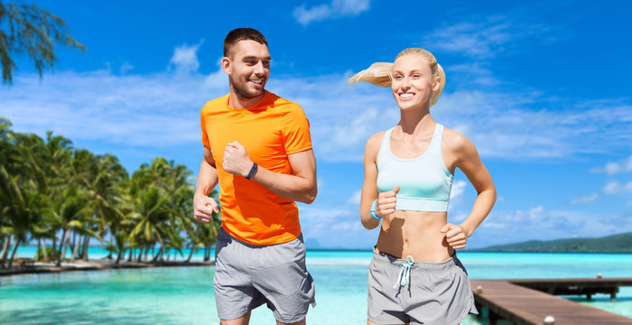 sport, healthy lifestyle and people concept - smiling couple with fitness trackers running at summer over city street on background