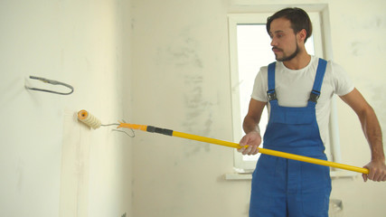 Repairman in uniform paints a wall in the flat