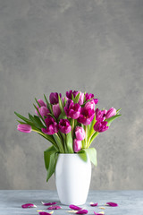 bouquet of tulips in white vase on stone grey background