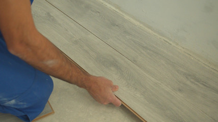 Close up, builder in uniform puts laminate on the floor 