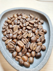 Coffee beans in a gray bowl on a white background.