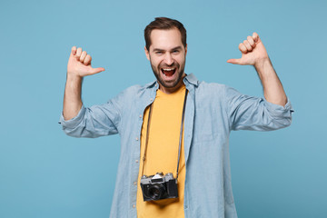 Funny traveler tourist man in yellow summer clothes with photo camera isolated on blue background. Male passenger traveling abroad on weekends. Air flight journey concept. Pointing thumbs on himself.