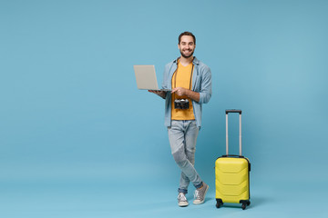 Smiling traveler tourist man in yellow clothes with photo camera suitcase isolated on blue...