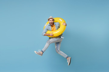 Fototapeta na wymiar Cheerful traveler tourist man in yellow casual summer clothes isolated on blue background. Male passenger traveling abroad on weekends. Air flight journey concept. Jumping, holding inflatable ring.