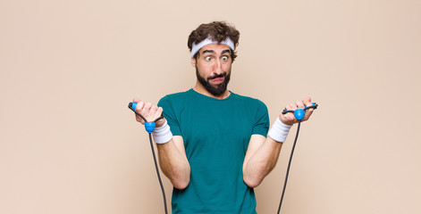 young cool sports man with a jump rope against flat wall