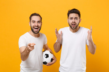 Shocked men guys friends in white t-shirt posing isolated on yellow background. Sport leisure concept. Mock up copy space. Cheer up support favorite team with soccer ball point index finger on camera.