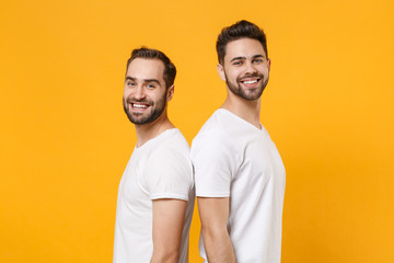 Smiling young men guys friends in white blank t-shirts posing isolated on yellow orange background...