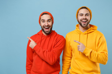 Two excited hipster men guys in fashion red yellow clothes posing isolated on pastel blue...