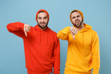 Naklejka premium Two displeased hipster men guys in fashion red yellow clothes posing isolated on pastel blue background studio portrait. People emotions lifestyle concept. Mock up copy space. Showing thumbs down.