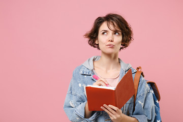 Pensive young woman student in denim clothes backpack isolated on pastel pink background in studio....