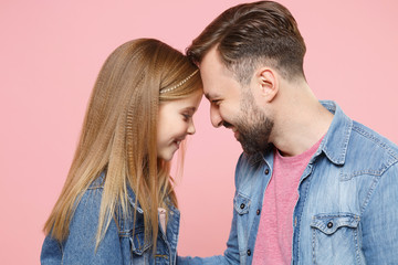 Side view of smiling bearded man in casual clothes with child baby girl. Father little kid daughter isolated on pastel pink background. Love family parenthood childhood concept. Touching foreheads.