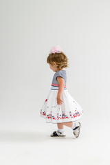 little girl of two years in a dress with a bow goes in profile over a light background