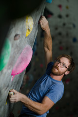 young handsome active bearded caucasian male in glasses climbing on wall in sport activity gym during bouldering workout train session