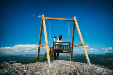 a woman takes a selfie while she is sitting on a wooden swing