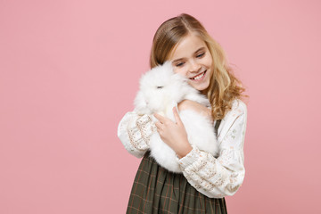 Little pretty blonde kid girl 11-12 years old in light spring dress hold fluffy white bunny rabbit...