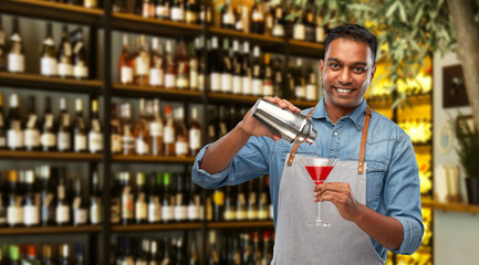 alcohol drinks, people and profession concept - indian barman in apron pouring cocktail from shaker...
