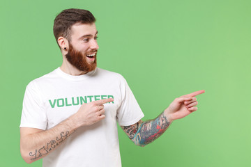 Excited young bearded man in white volunteer t-shirt isolated on pastel green background studio...