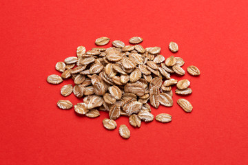 Pile of oat rye flakes on red color background