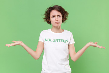 Displeased young brunette woman in white volunteer t-shirt isolated on pastel green wall background...