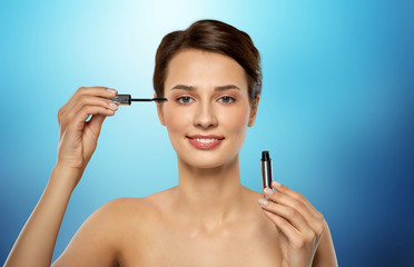 Fototapeta premium beauty, makeup and cosmetics concept - beautiful young woman applying mascara over blue background