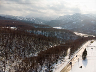 Slopes of Tokiwa with trees and a road by the side of it with some vehicle for scale in Hokkaido during early winter with powerlines in photo 