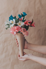 Hand hold bouquet of flowers. Unrecognizable woman hands holding a beautiful bouquet of colorful spring flowers against crafty brown paper background