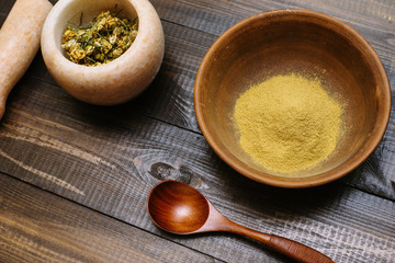 Marble mortar with dried chamomile for natural cosmetics. Clay bowl with yellow powder or clay and flowers on a wooden background. Flat lay