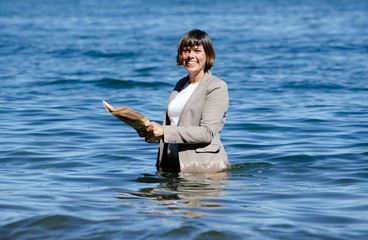 Elegant Business Woman with Suit Standing in the Water and Reading a Newspaper.