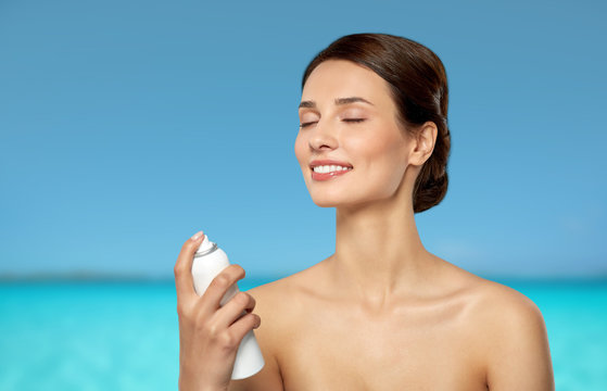 Beauty, Bodycare And People Concept - Beautiful Young Woman Applying Facial Spray Or Mist To Her Face Skin Over Blue Sea And Sky Background