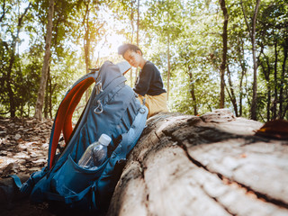 Trekking and camping adventure concept from blue backpack with tired women sitting rest on a log while walk travel nature in forest.