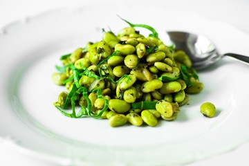 Boiled fava beans with spoon on white plate, close-up.